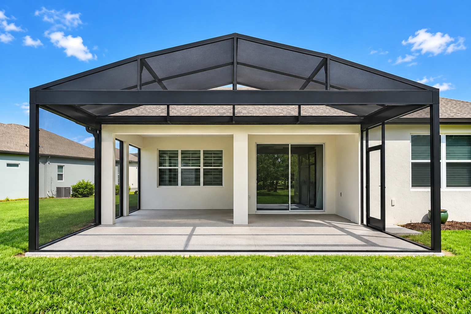 A black-framed screened patio enclosure with a peaked roof covers a bare concrete patio beside a house.