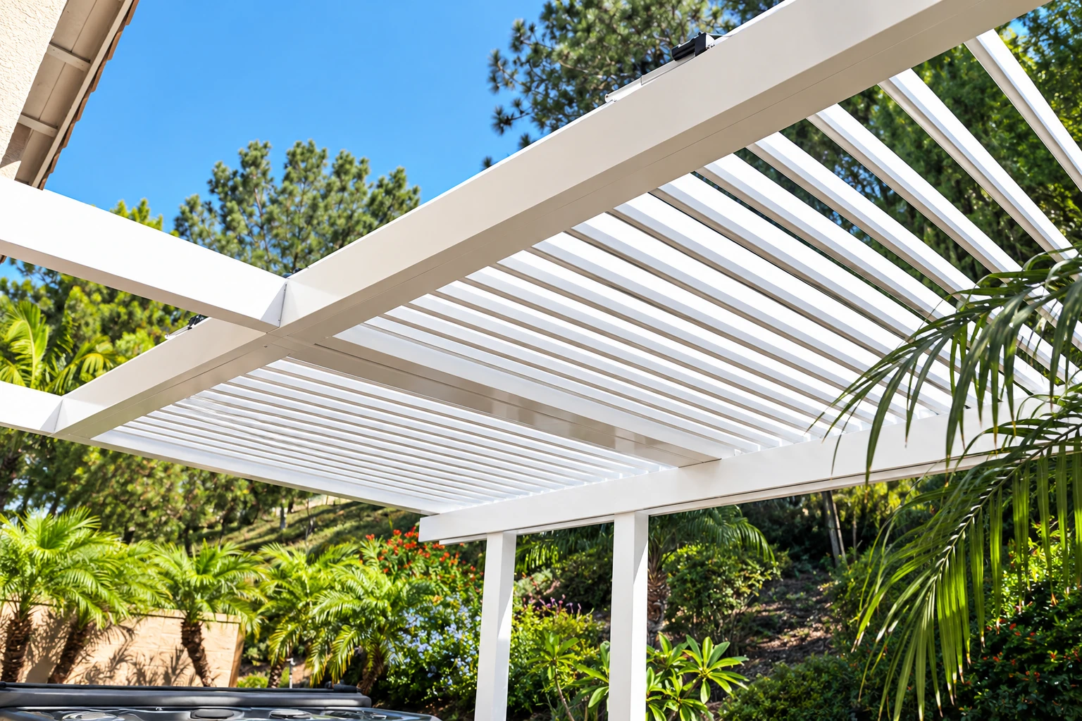 White patio cover with open slatted roofing extends over an outdoor seating area amid trees.